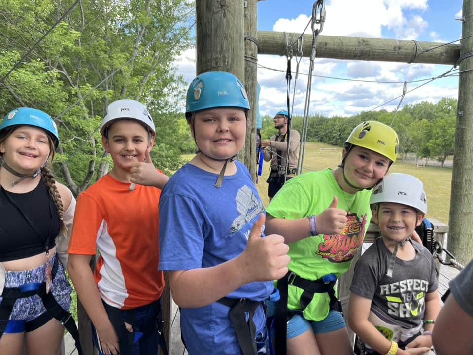 Campers giving thumbs up in climbing helmets at the ropes course