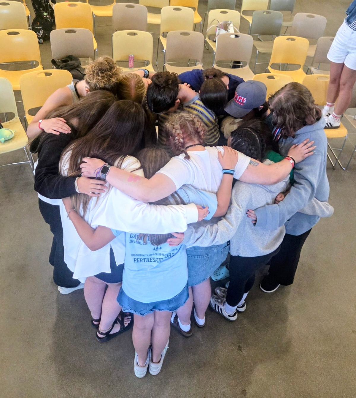 A group of Camp Perthes girls in a tight circle with arms wrapped around each other's shoulders, seen from above